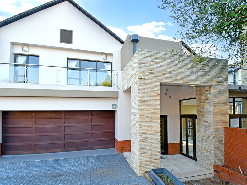 Modern double-story home exterior featuring stone cladding, a paved driveway, a double garage, and a glass-balustraded balcony.
