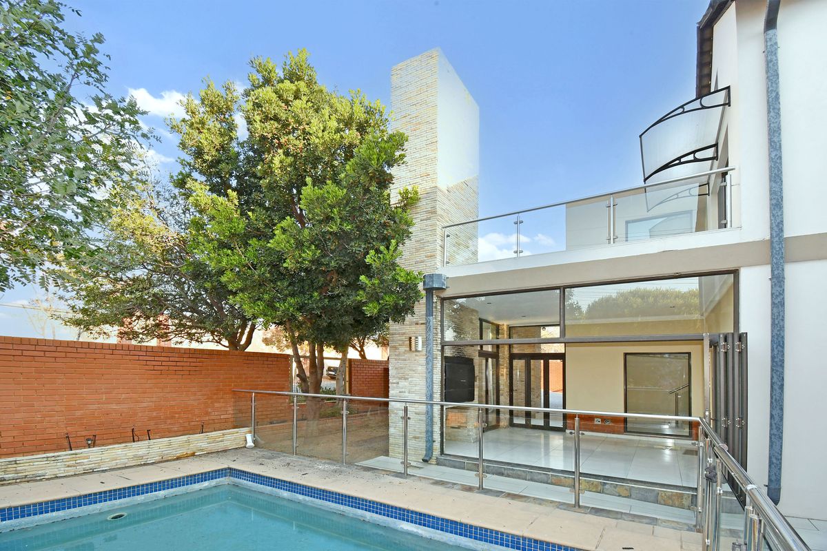 Rear exterior view featuring a swimming pool, glass balustrades, stone-clad chimney, and a spacious patio area with large sliding glass doors.