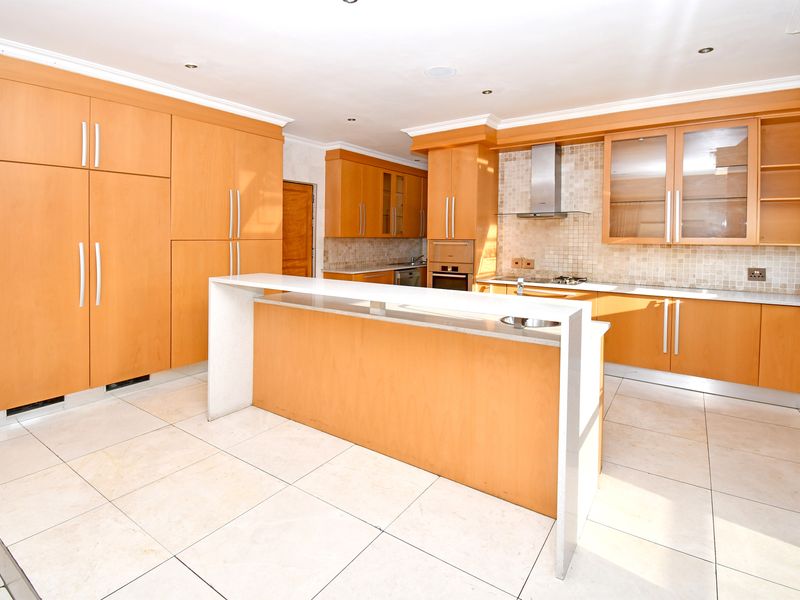 A spacious kitchen featuring light wood cabinetry, a central island with a stone countertop, tiled backsplash, and integrated appliances.