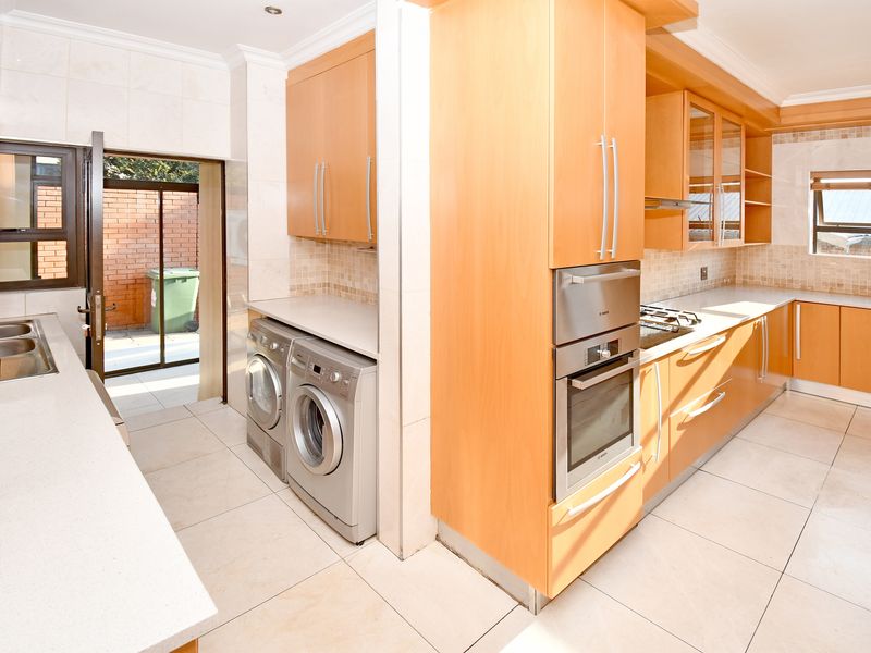 A functional kitchen featuring light wood cabinetry, stone countertops, built-in oven, gas hob, and an integrated laundry area with direct access to the rear exterior.
