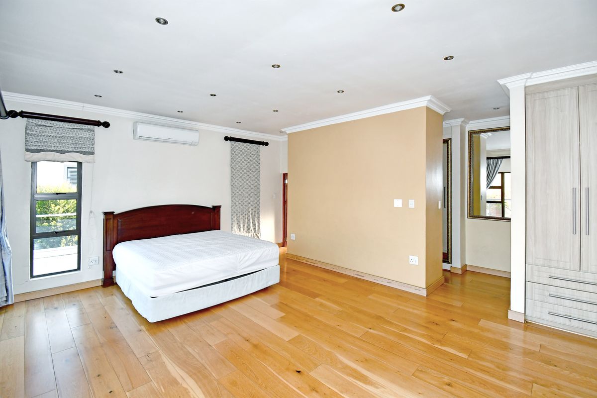 Spacious bedroom featuring timber flooring, recessed downlighting, split-system air conditioning, and built-in cabinetry with a neutral color palette.