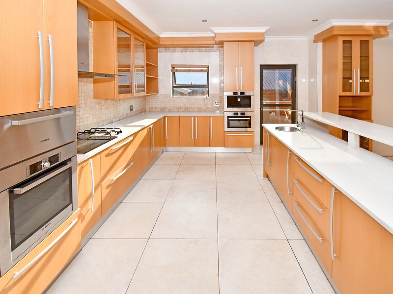 Spacious modern kitchen featuring light wood cabinetry, stone countertops, integrated Bosch appliances, gas hob, and tiled flooring throughout.