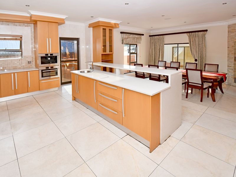 Spacious open-plan kitchen and dining area featuring light wood cabinetry, stone countertops, a central island, and a stone-clad fireplace.