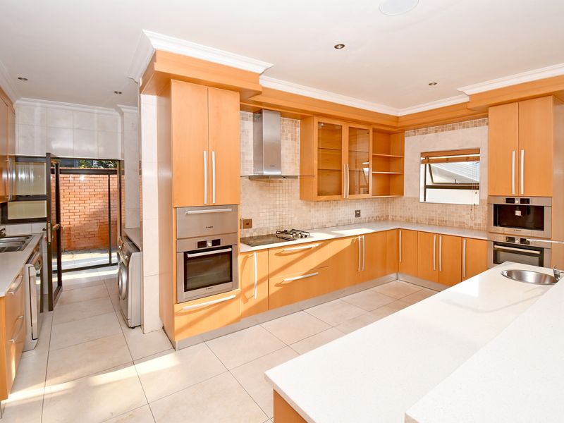Spacious kitchen featuring light wood cabinetry, stone countertops, integrated stainless steel appliances, and tiled flooring with a connected scullery area.