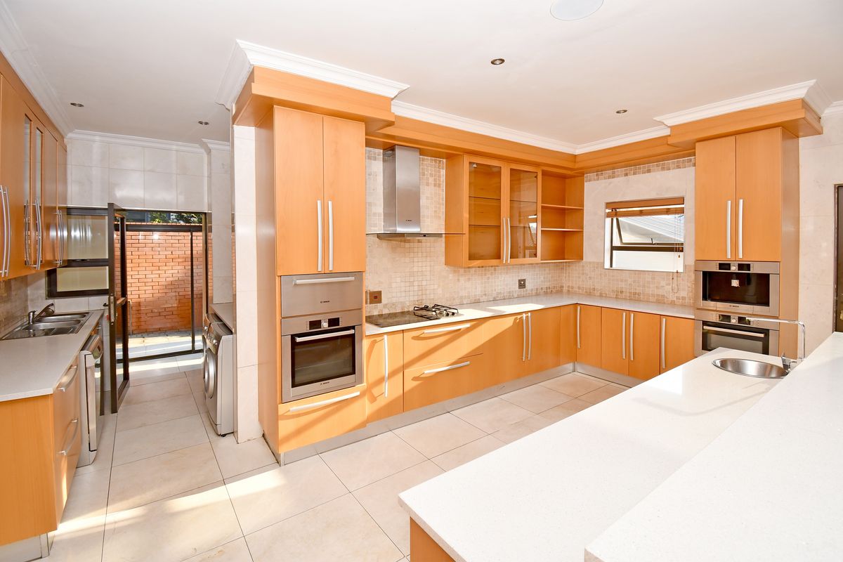 Spacious kitchen featuring light wood cabinetry, stone countertops, integrated stainless steel appliances, and tiled flooring with a connected scullery area.