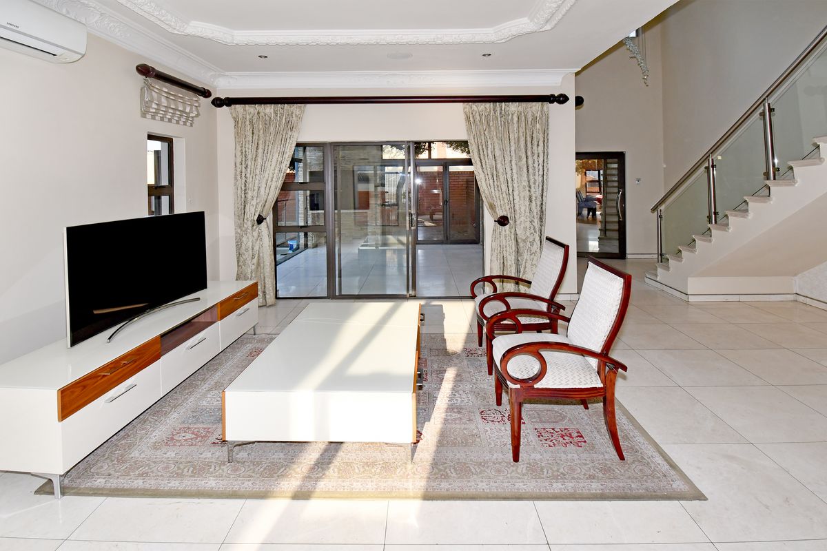 Spacious living room featuring tiled floors, decorative ceiling cornices, and a modern staircase with glass balustrades, leading out to a patio area.