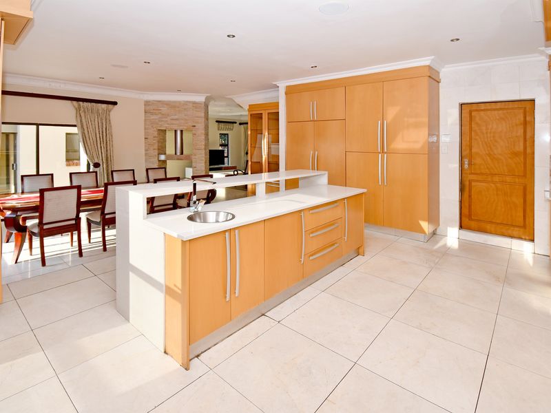 Spacious open-plan kitchen and dining area featuring light wood cabinetry, a central island with sink, and neutral tiled flooring throughout.