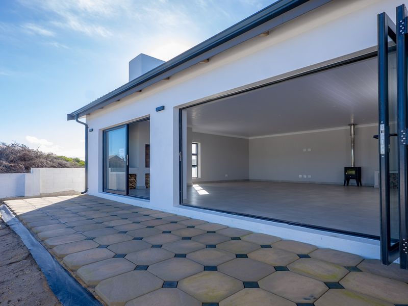 Spacious outdoor patio featuring paved flooring and large bi-fold doors opening into a bright, open-plan living area with a modern fireplace.