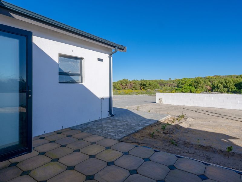 Rear view of the property featuring a paved patio area, modern sliding door access, and a low-maintenance garden space with a boundary wall.