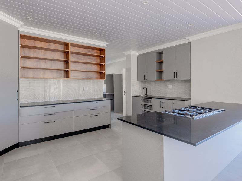 Modern kitchen featuring sleek grey cabinetry, stone countertops, a central island with a gas hob, and elegant tongue and groove ceiling detailing.