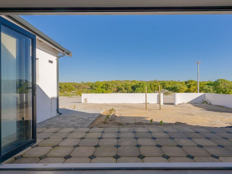 A paved patio area featuring modern bi-fold doors, leading out to an open, unfinished garden space with a boundary wall.