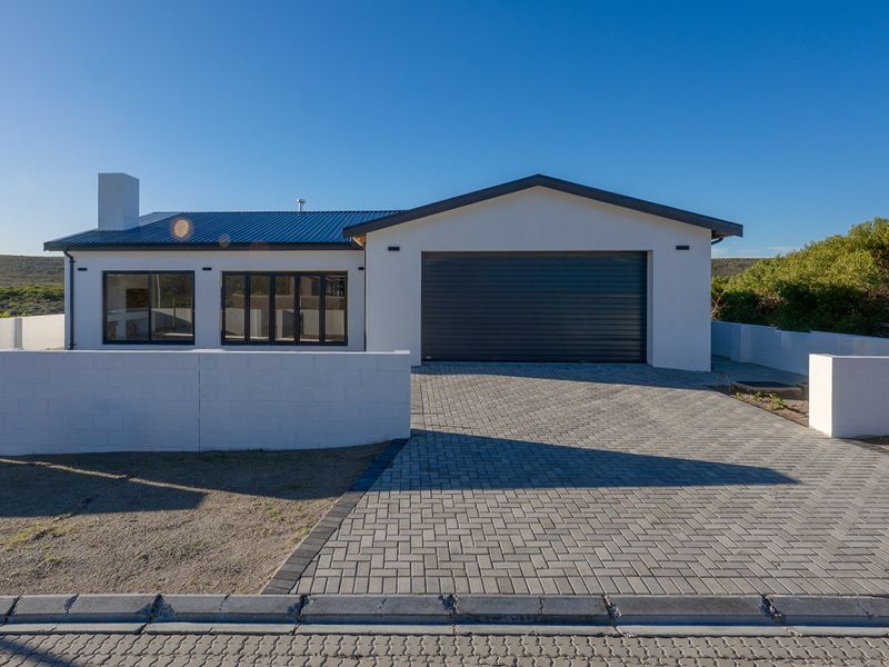 Front elevation of a modern single-story house featuring a paved driveway, integrated garage, and clean white exterior finishes under a metal roof.