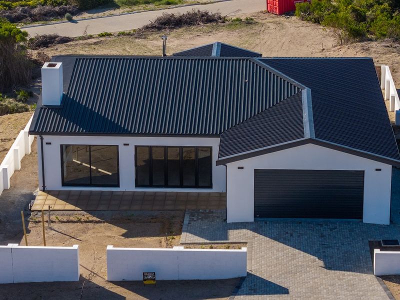 Aerial view of a modern single-story house featuring a dark corrugated metal roof, paved driveway, and a secure boundary wall.