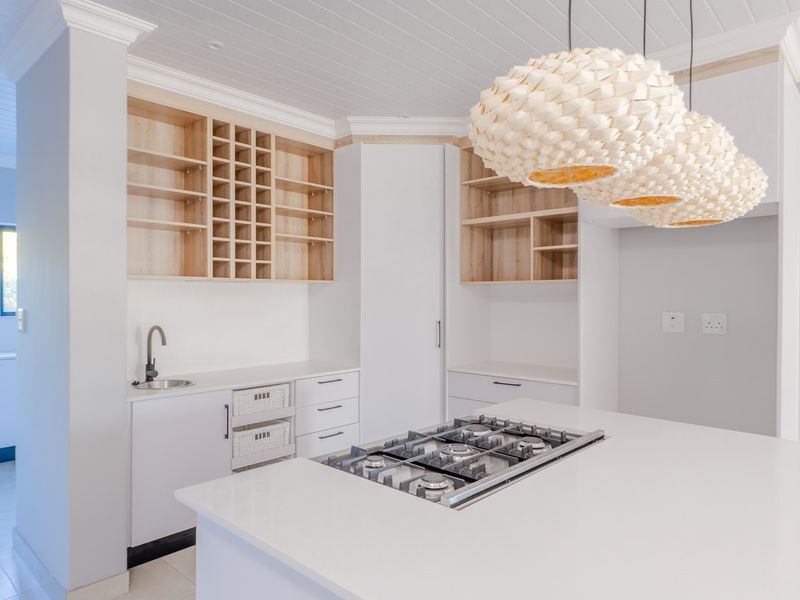 Modern kitchen featuring a central island with a gas cooktop, extensive built-in cabinetry, open shelving, and a sleek undermount sink.
