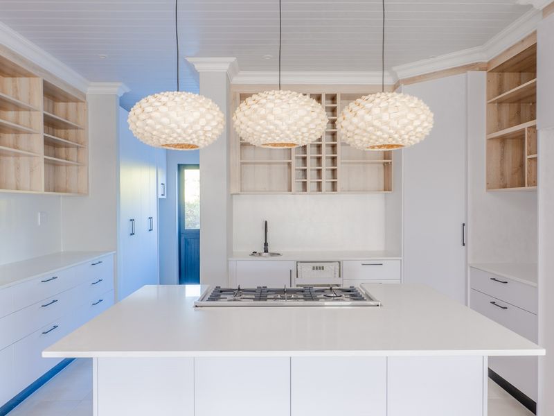 Modern kitchen featuring a central island with a gas cooktop, extensive built-in cabinetry, open shelving, and a clean, minimalist aesthetic.