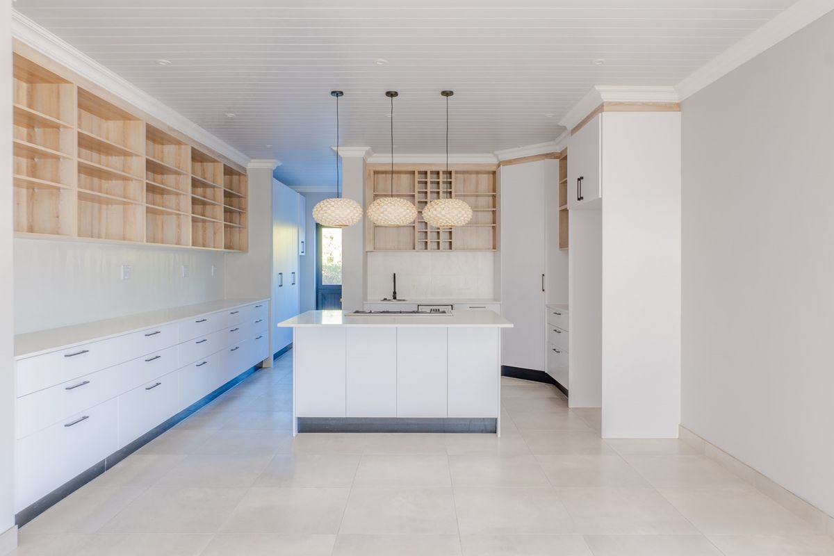 Modern, spacious kitchen featuring a central island, extensive built-in cabinetry, open shelving, and sleek tiled flooring under a classic tongue and groove ceiling.