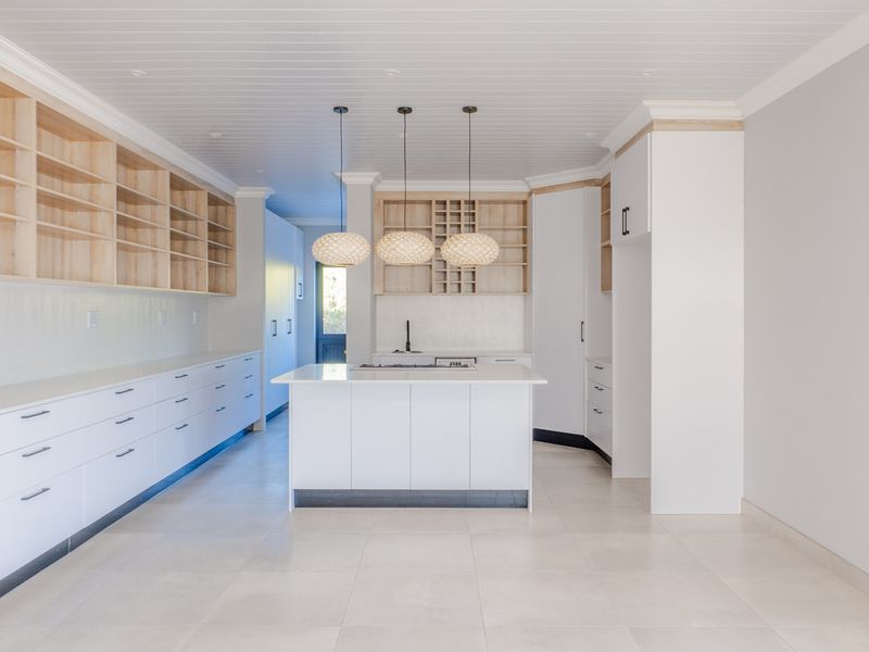 Modern, spacious kitchen featuring a central island, extensive built-in cabinetry, open shelving, and sleek tiled flooring under a classic tongue and groove ceiling.