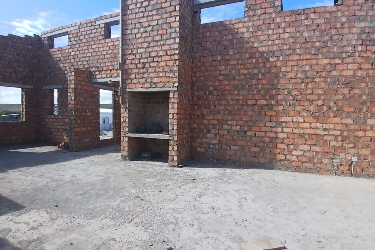 An unfinished interior space featuring exposed brick walls, a built-in fireplace, and concrete flooring, currently under construction.