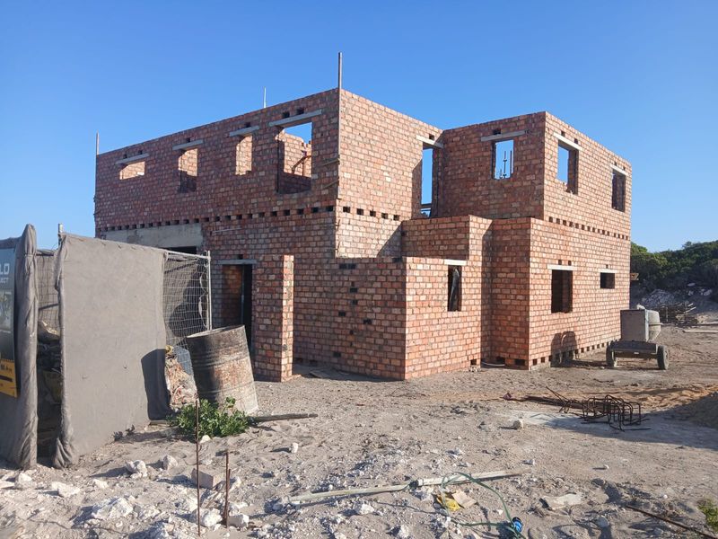 A construction site view showing the structural brickwork shell of a two-story house in the early stages of development.