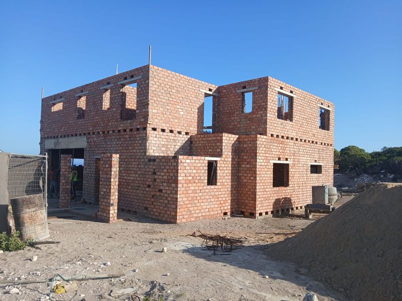 A two-story residential property under construction, featuring exposed brick masonry walls and structural openings on a cleared building site.
