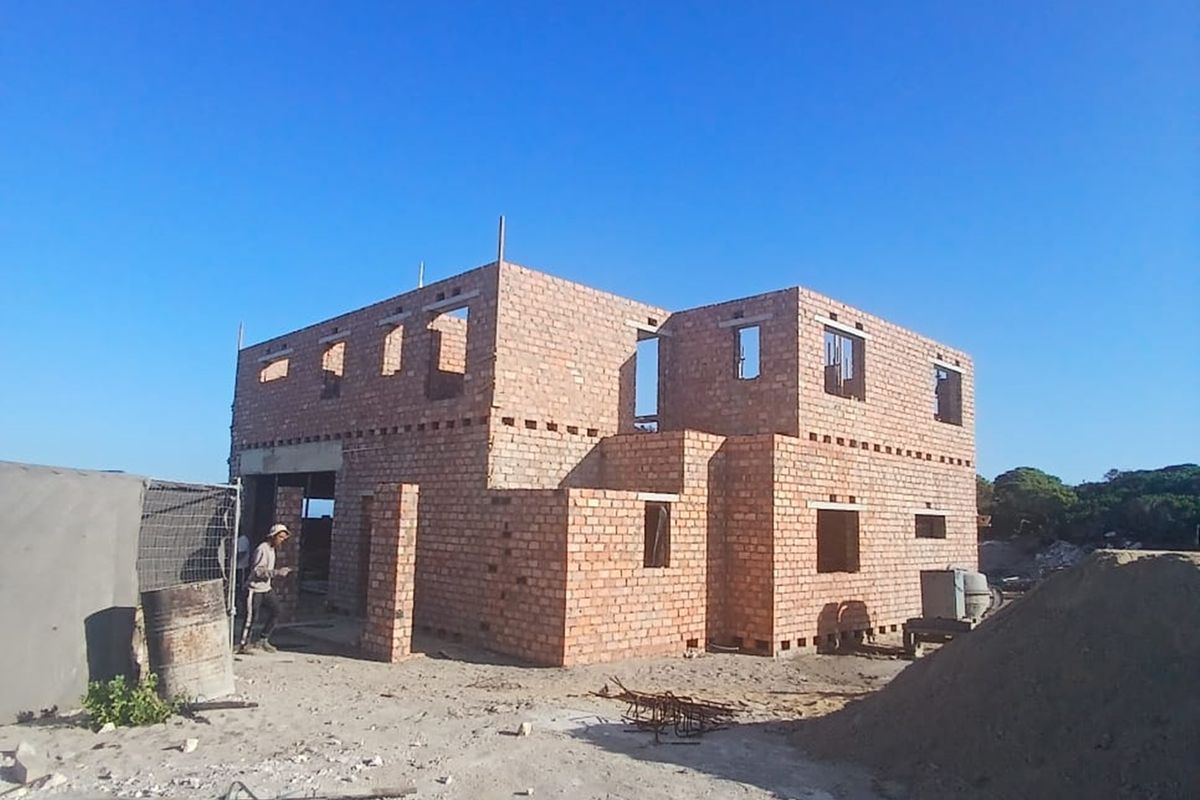 A two-story residential property currently under construction, featuring exposed brick masonry and unfinished structural openings on a sandy building site.