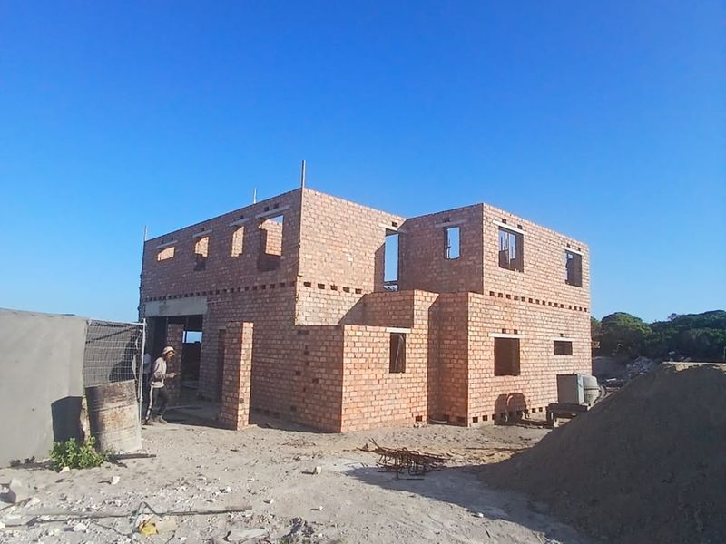 A two-story residential property currently under construction, featuring exposed brick masonry and unfinished structural openings on a sandy building site.