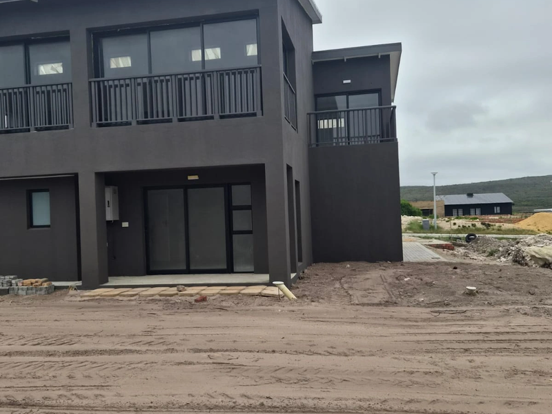 Rear view of a modern two-story house featuring dark exterior cladding, sliding glass doors, and upper-level balconies, currently surrounded by unfinished landscaping.