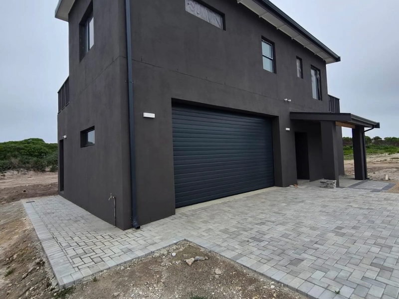 Modern double-story home exterior featuring a dark rendered facade, automated garage door, paved driveway, and covered entrance area.