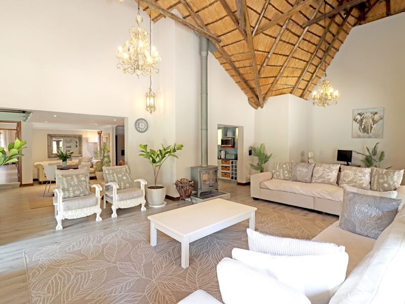 Spacious open-plan living area featuring a high vaulted thatched ceiling with exposed rafters, a central freestanding fireplace, and light-toned laminate flooring.