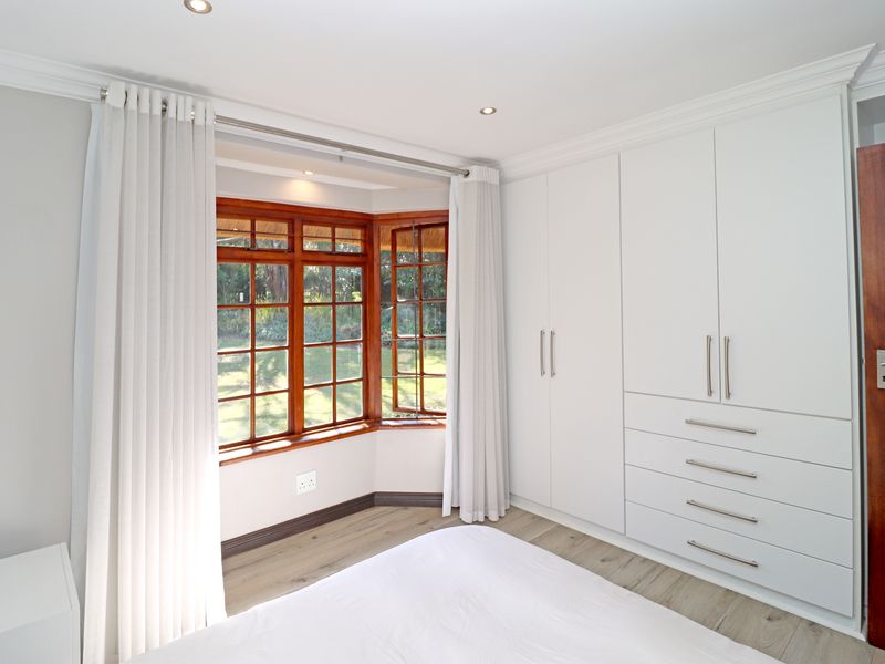 A bright bedroom featuring built-in white cabinetry, a charming timber-framed bay window, and modern laminate flooring with recessed lighting.