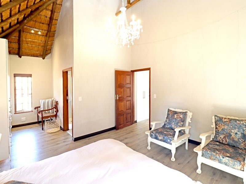 Spacious bedroom featuring a high thatched ceiling with exposed timber rafters, laminate flooring, and a classic chandelier.