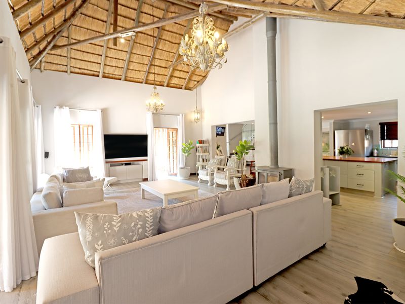 Spacious open-plan living area featuring a high vaulted thatched ceiling with exposed rafters, a central fireplace, and seamless flow into the kitchen.