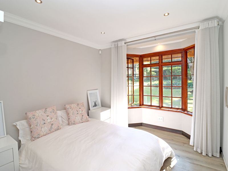 A bright and well-maintained bedroom featuring a charming bay window with timber frames, laminate flooring, and built-in storage.