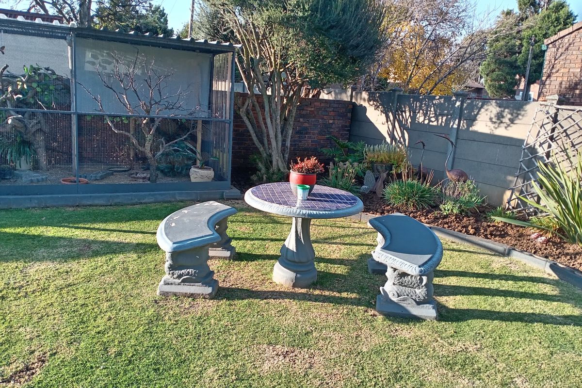 A private rear garden featuring a large wire enclosure, established trees, and a paved seating area with a stone table and benches.