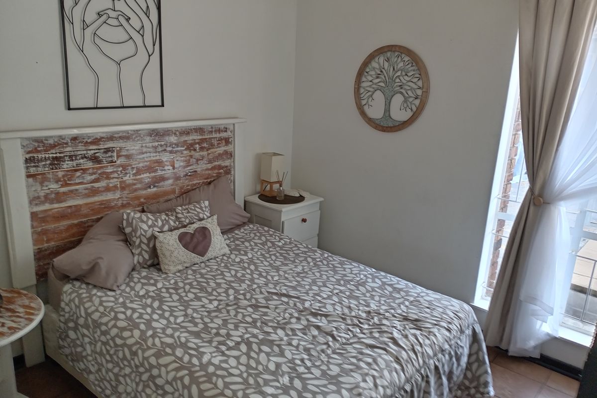 A cozy bedroom featuring tiled flooring, a rustic wooden headboard, and a window with curtain treatments.