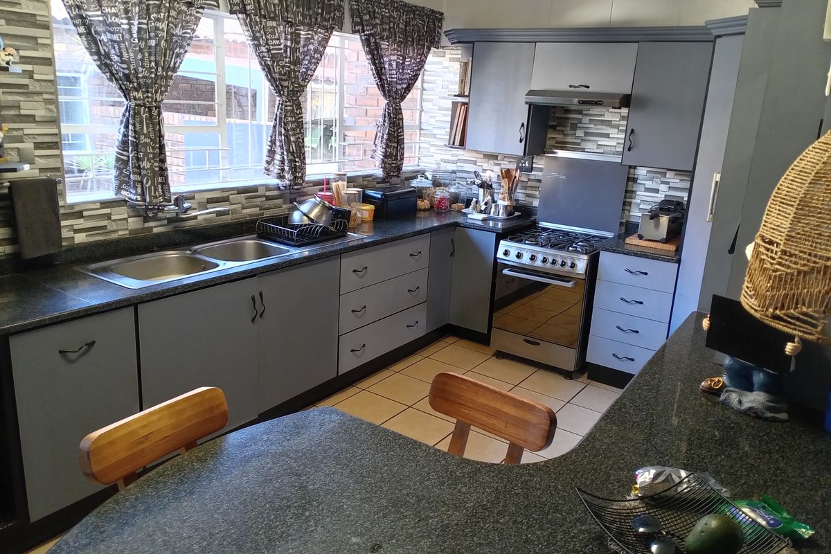 A functional kitchen featuring grey cabinetry, granite countertops, a gas stove with extractor fan, and a double basin sink.