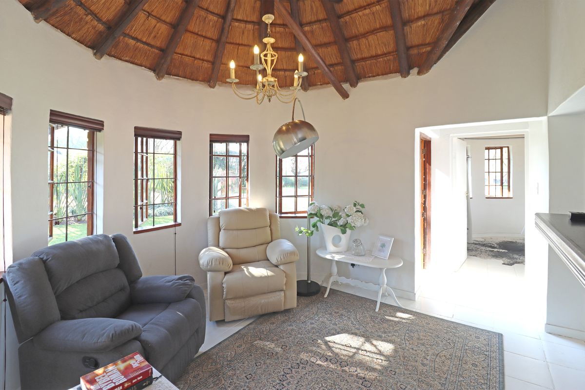 A circular living room featuring a traditional thatched roof with exposed timber rafters, large timber-framed windows, and tiled flooring.