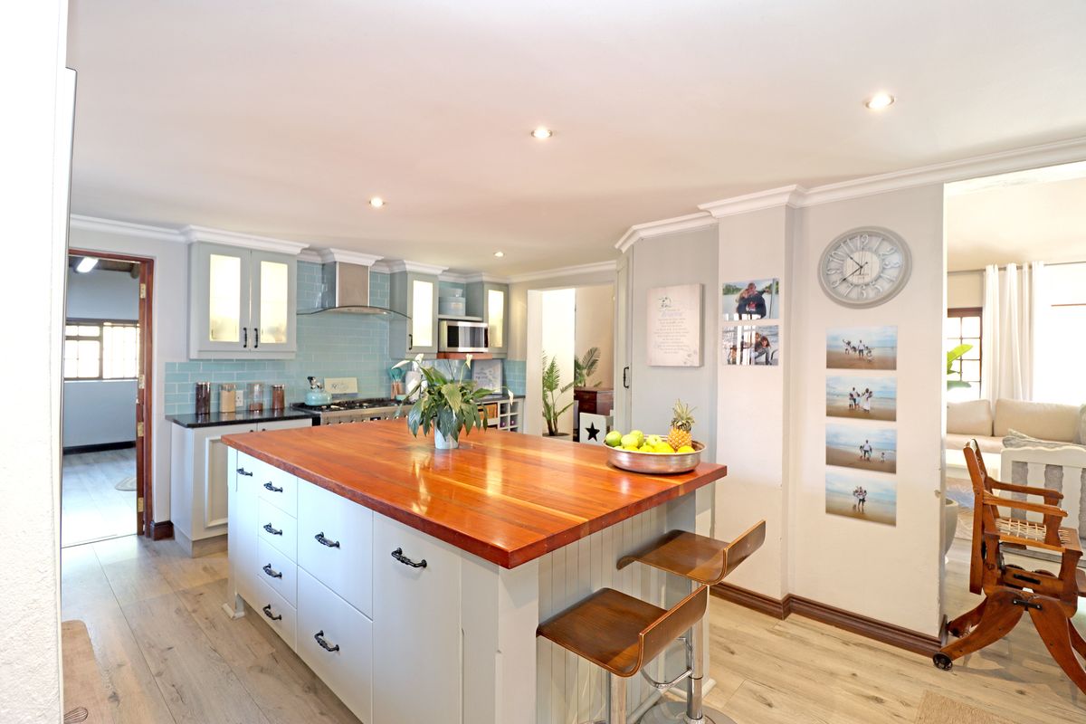 A well-appointed kitchen featuring a large central island with a wooden countertop, light-toned cabinetry, a tiled backsplash, and modern recessed lighting.