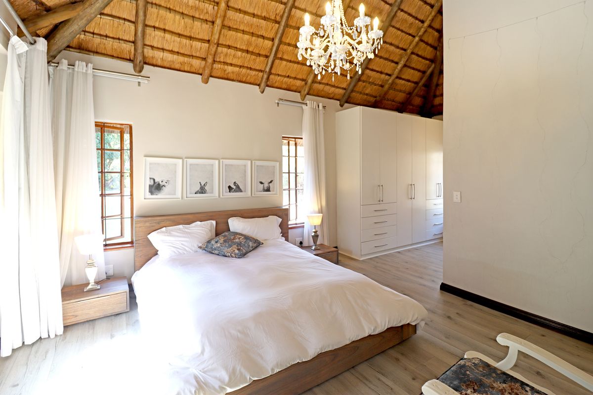 Spacious bedroom featuring a high vaulted thatch ceiling with exposed timber rafters, built-in cabinetry, and modern laminate flooring.
