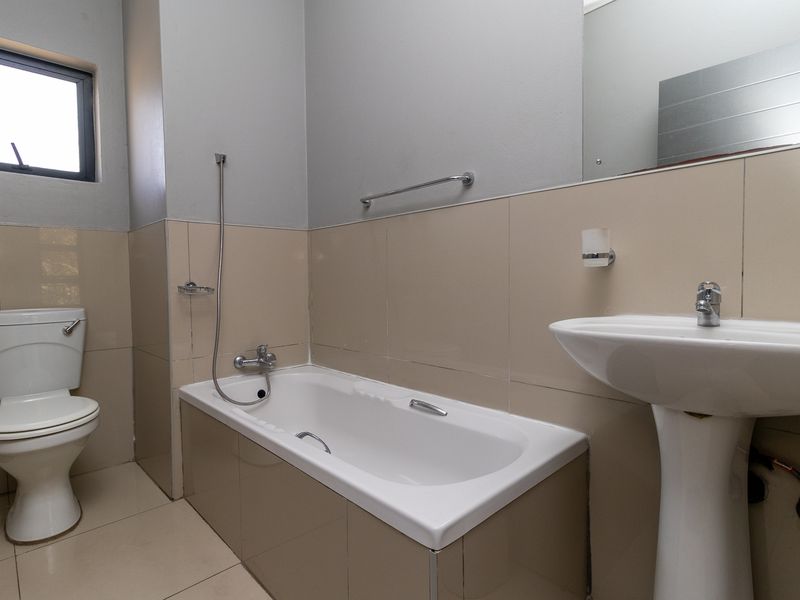A functional bathroom featuring a bathtub, pedestal basin, and toilet with neutral wall tiling and a large wall-mounted mirror.