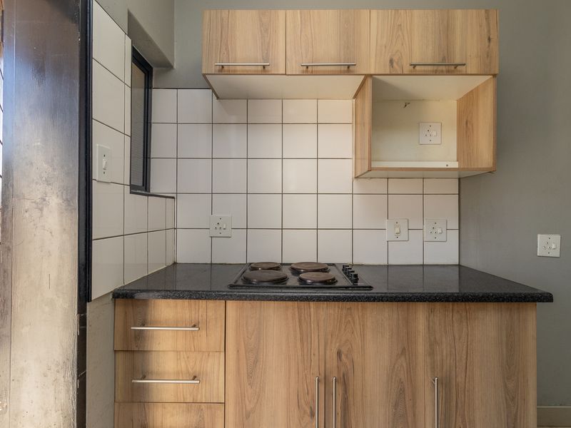 A compact kitchen featuring wood-look cabinetry, dark laminate countertops, a built-in electric hob, and a clean white tiled backsplash.