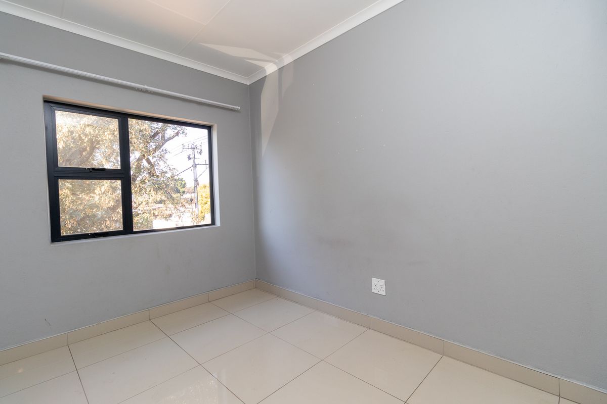 A clean, empty bedroom featuring neutral grey walls, tiled flooring, and an aluminium-framed window, providing a blank canvas for personalization.