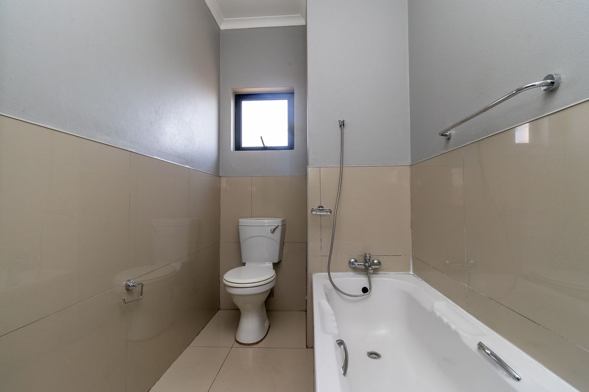 A functional bathroom featuring a bathtub with a handheld shower mixer, a toilet, and neutral wall and floor tiling.
