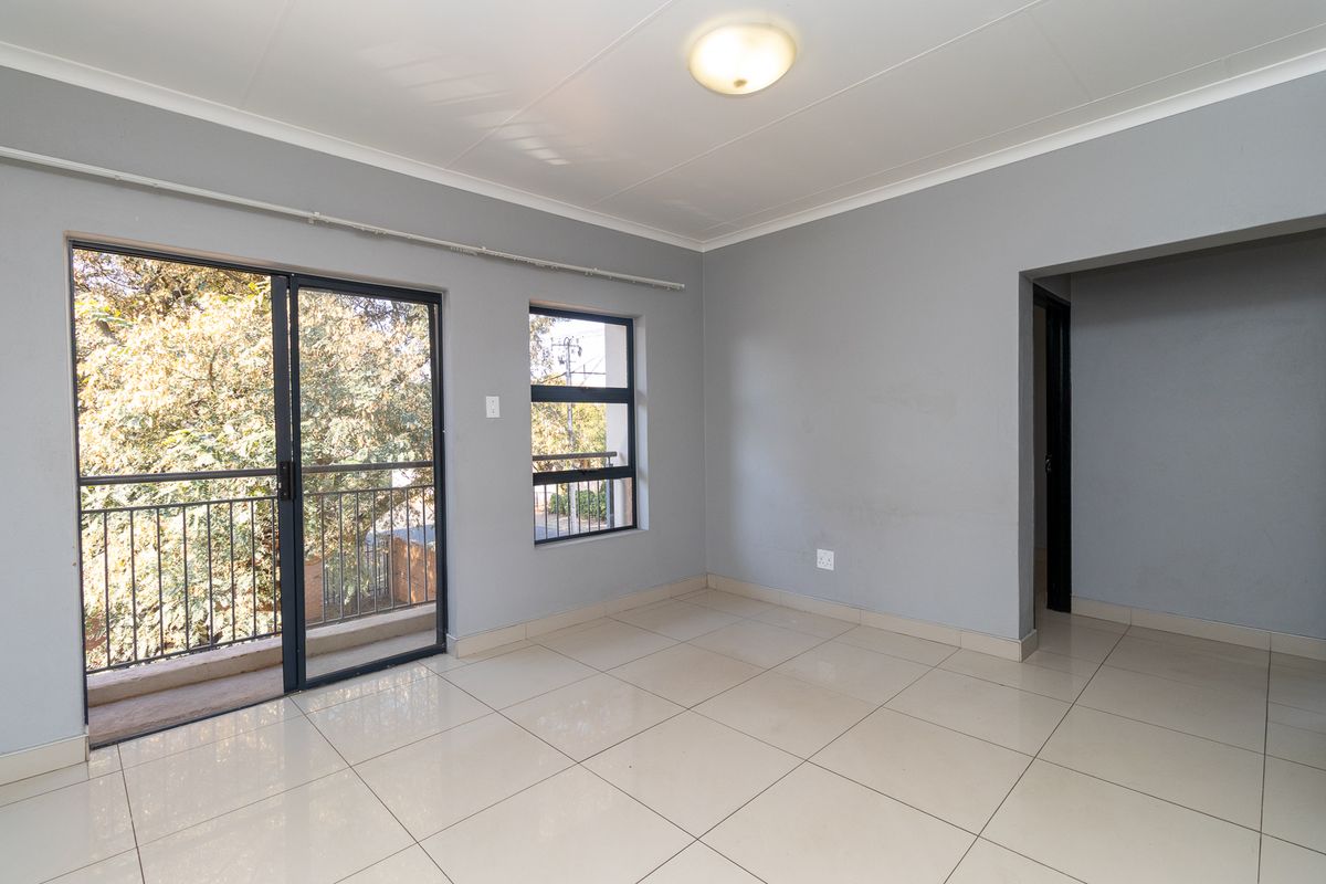 A bright, empty living area featuring neutral grey walls, tiled flooring, and a sliding glass door providing access to a private balcony.