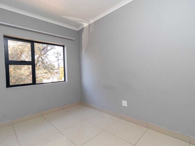 A clean, empty bedroom featuring neutral grey walls, tiled flooring, and an aluminium-framed window, providing a blank canvas for personalization.