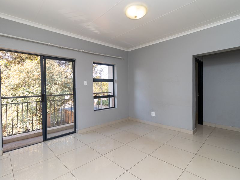 A bright, empty living area featuring neutral grey walls, tiled flooring, and a sliding glass door providing access to a private balcony.