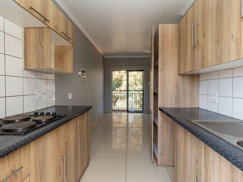 Modern galley-style kitchen featuring light wood-grain cabinetry, dark countertops, electric hob, and tiled flooring, leading to a bright balcony area.