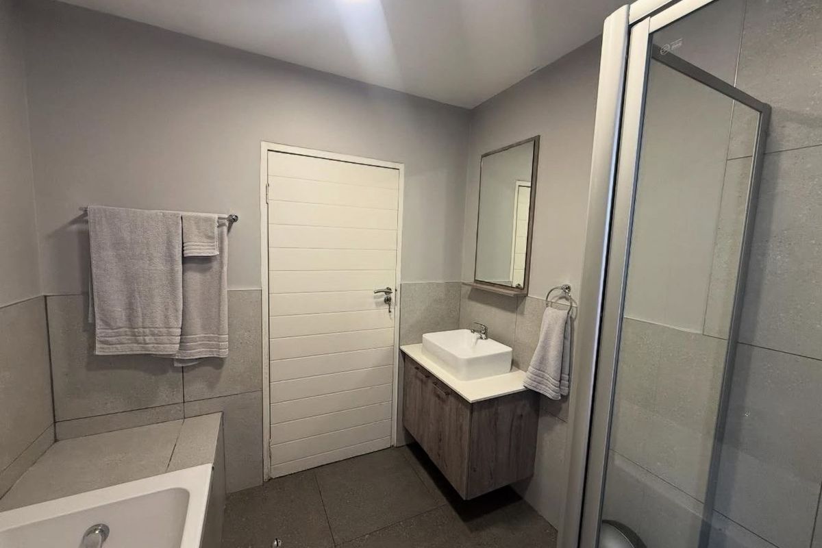 Modern bathroom featuring a floating vanity with vessel sink, glass-enclosed shower, and separate bathtub with neutral grey wall and floor tiling.
