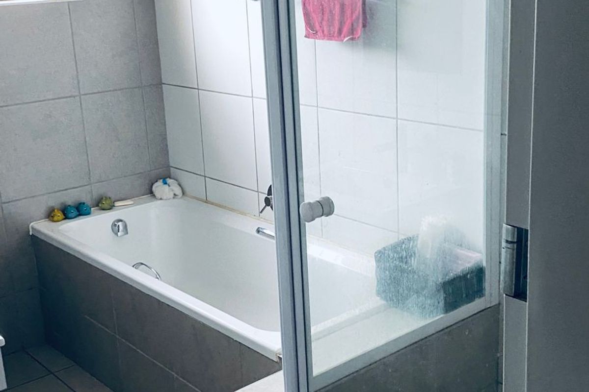 A functional bathroom featuring a built-in bathtub, a separate glass-enclosed shower, and neutral wall and floor tiling.