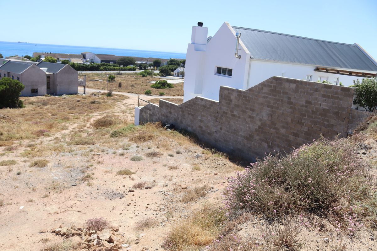View of a residential property exterior featuring a concrete block boundary wall, metal roofing, and surrounding coastal landscape.